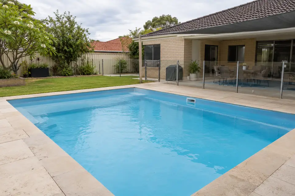 Clean backyard pool with clear blue water beside a brick home